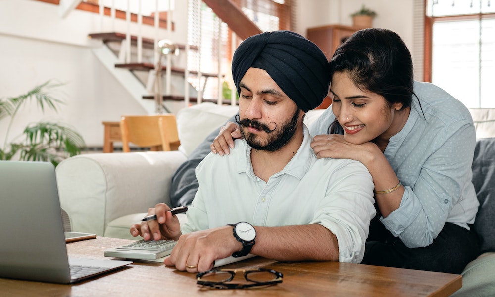 Cheerful-ethnic-couple-using-calculator-while-sitting-at-table