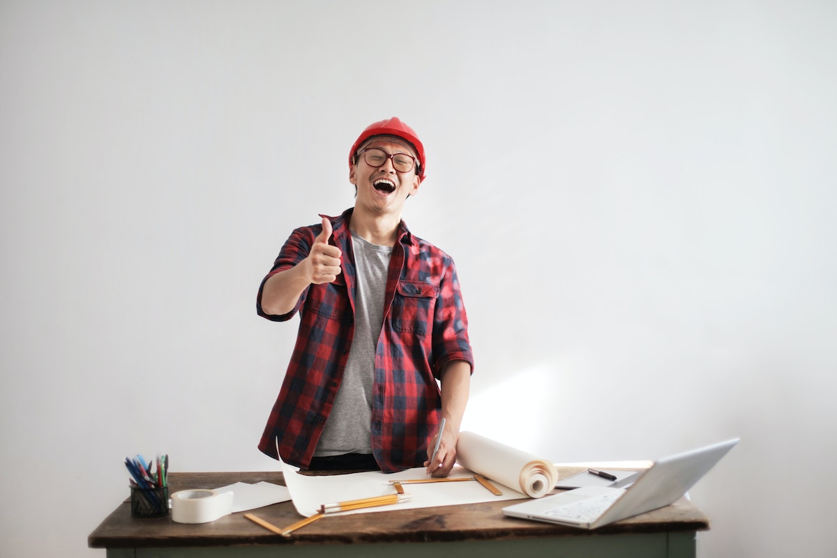 Laughing-male-constructor-showing-thumb-up-at-working-desk